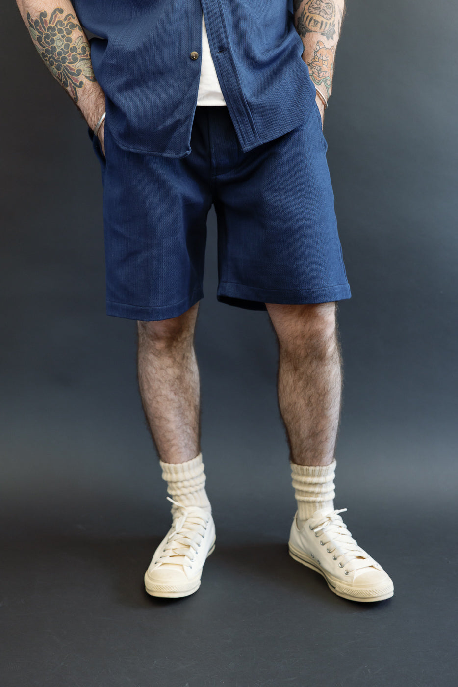 Full-body front view of male model in navy corduroy shorts, white tee, and cream sneakers.