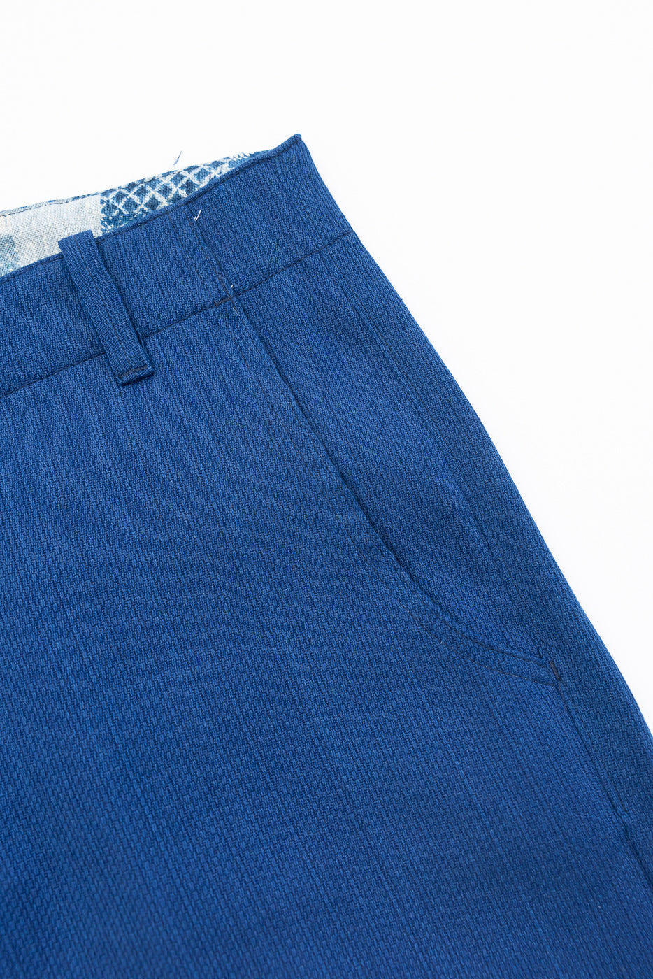 Close-up of blue trousers front, showing waistband, belt loop, and textured fabric detail