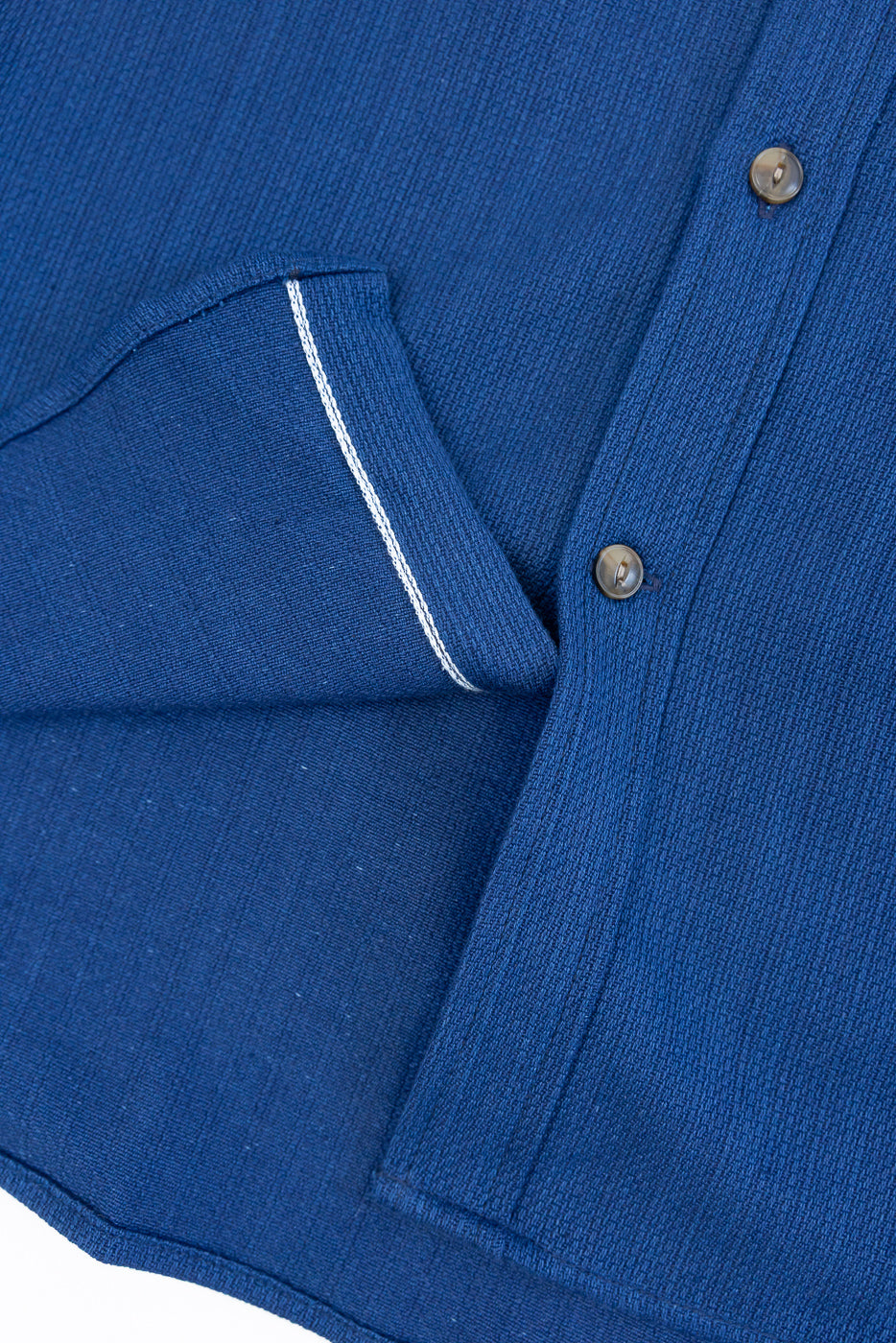 Close-up front view of blue button-up shirt showing chest pocket with white contrast stitching, fabric texture, and buttons