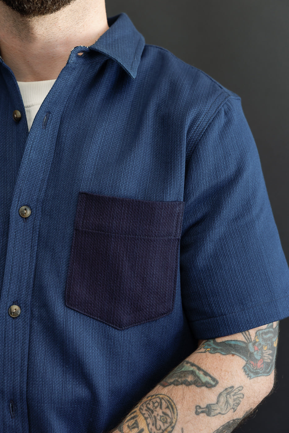 Close-up front view of male model in blue short-sleeve shirt with contrast pocket, buttons, and collar detail
