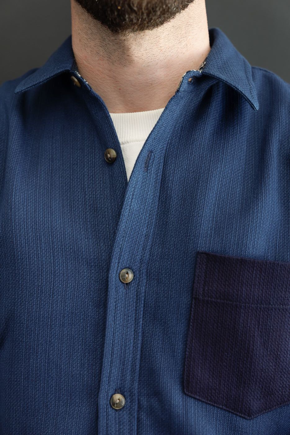 Close-up front view of navy shirt with textured fabric, buttons, and chest pocket, worn by male model.