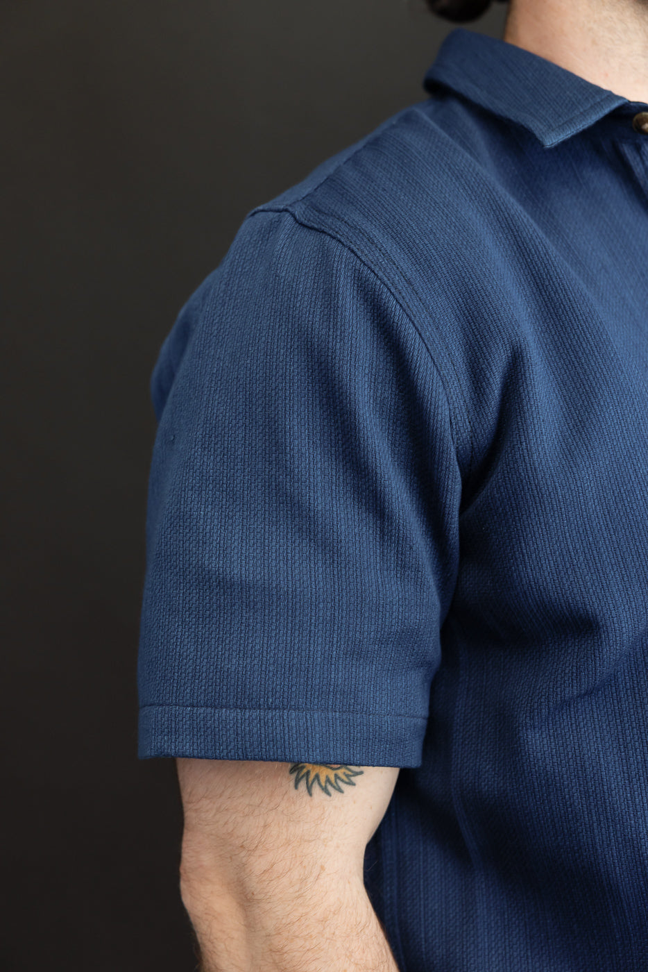 Close-up of navy polo shirt sleeve, showing texture and hem, worn by male model with athletic build.