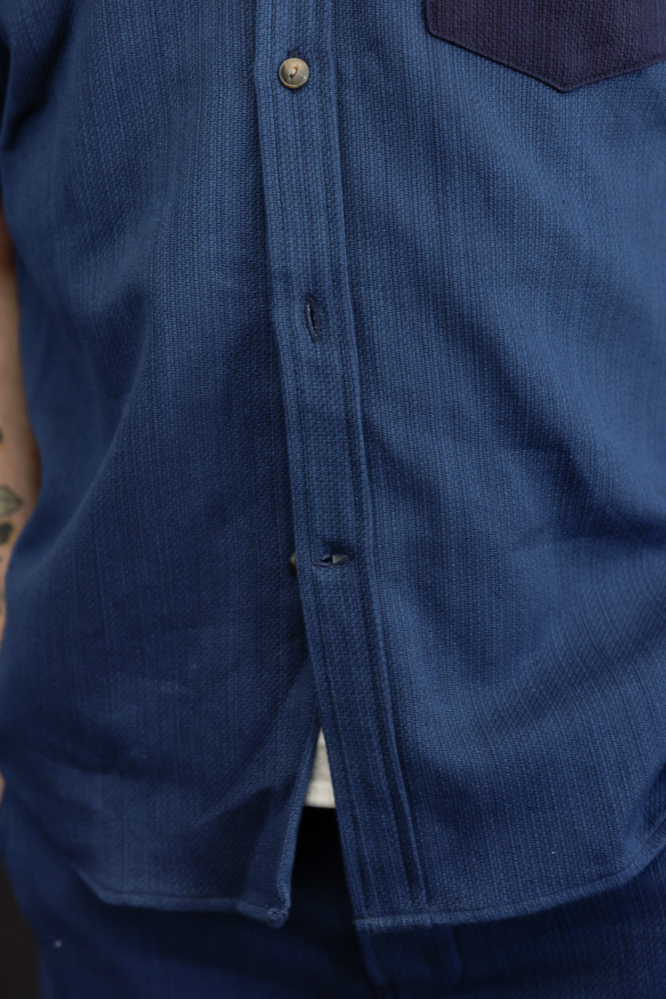 Close-up front view of navy shirt, showing button placket and fabric texture, worn by male model.