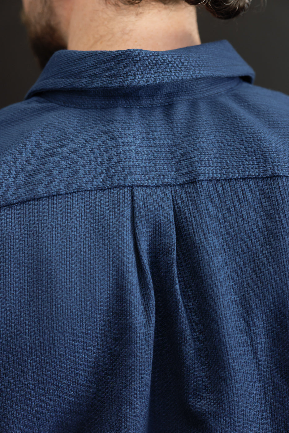 Back view close-up of navy shirt, showing collar and pleat detail, worn by male model