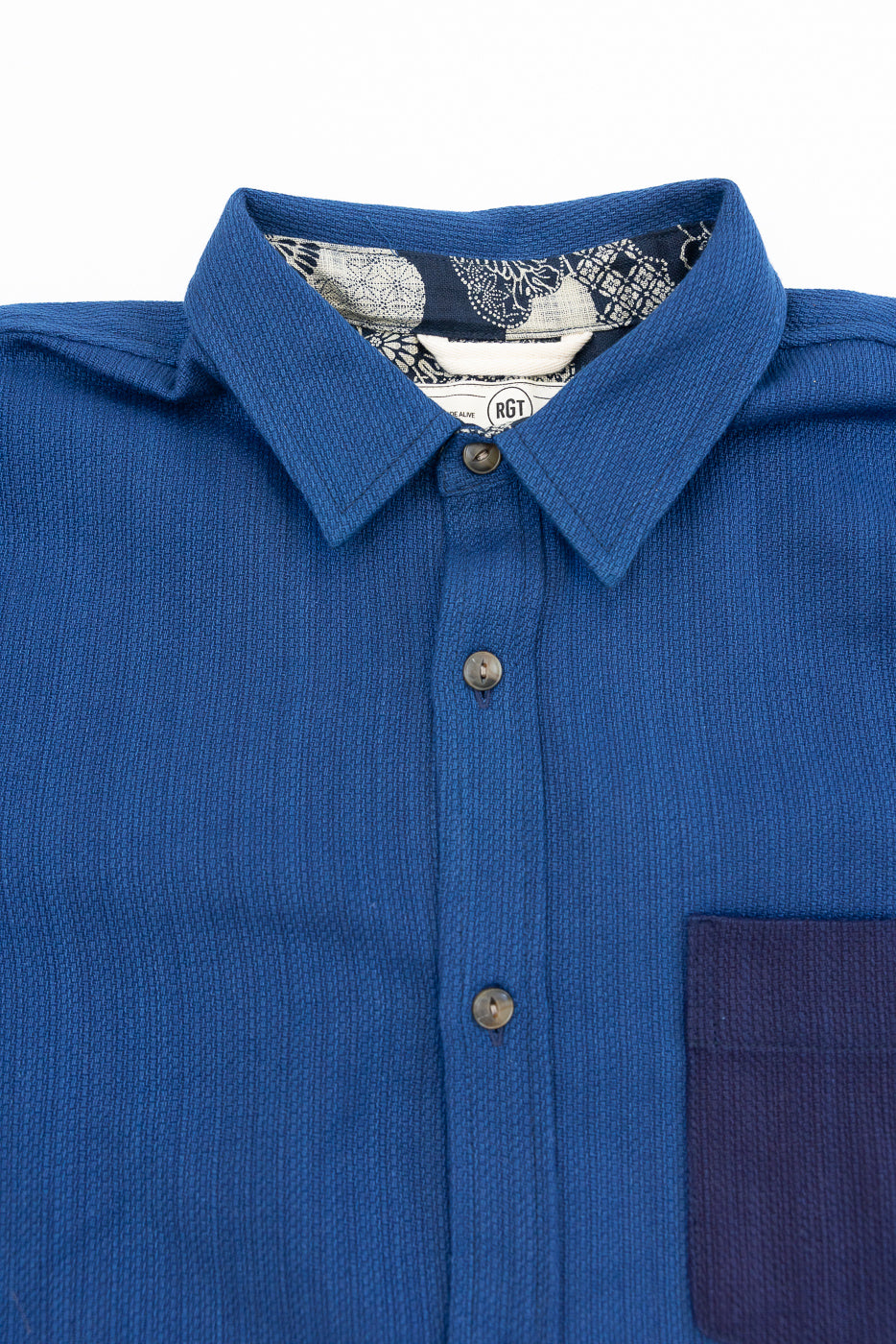 Close-up front view of blue textured shirt with patterned collar lining, buttons, and chest pocket