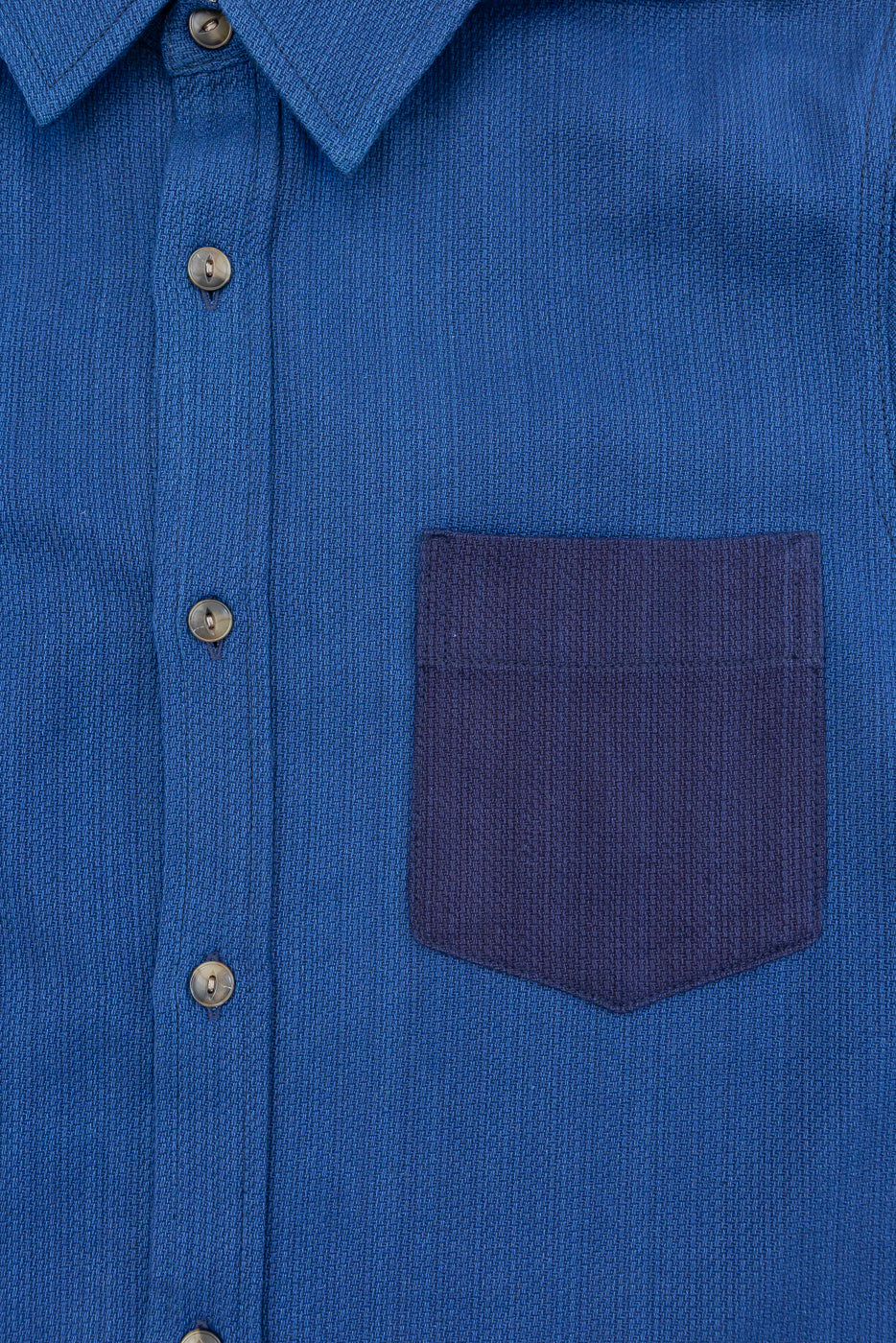 Close-up front view of blue button-up shirt with contrast pocket, showing collar, buttons, and textured fabric
