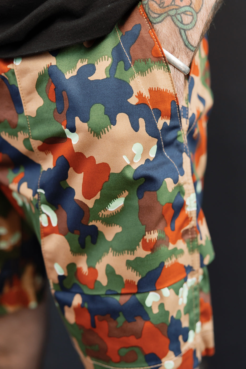 Close-up front view of men's camo shorts with multi-color pattern, side pocket, and stitching detail on athletic build model