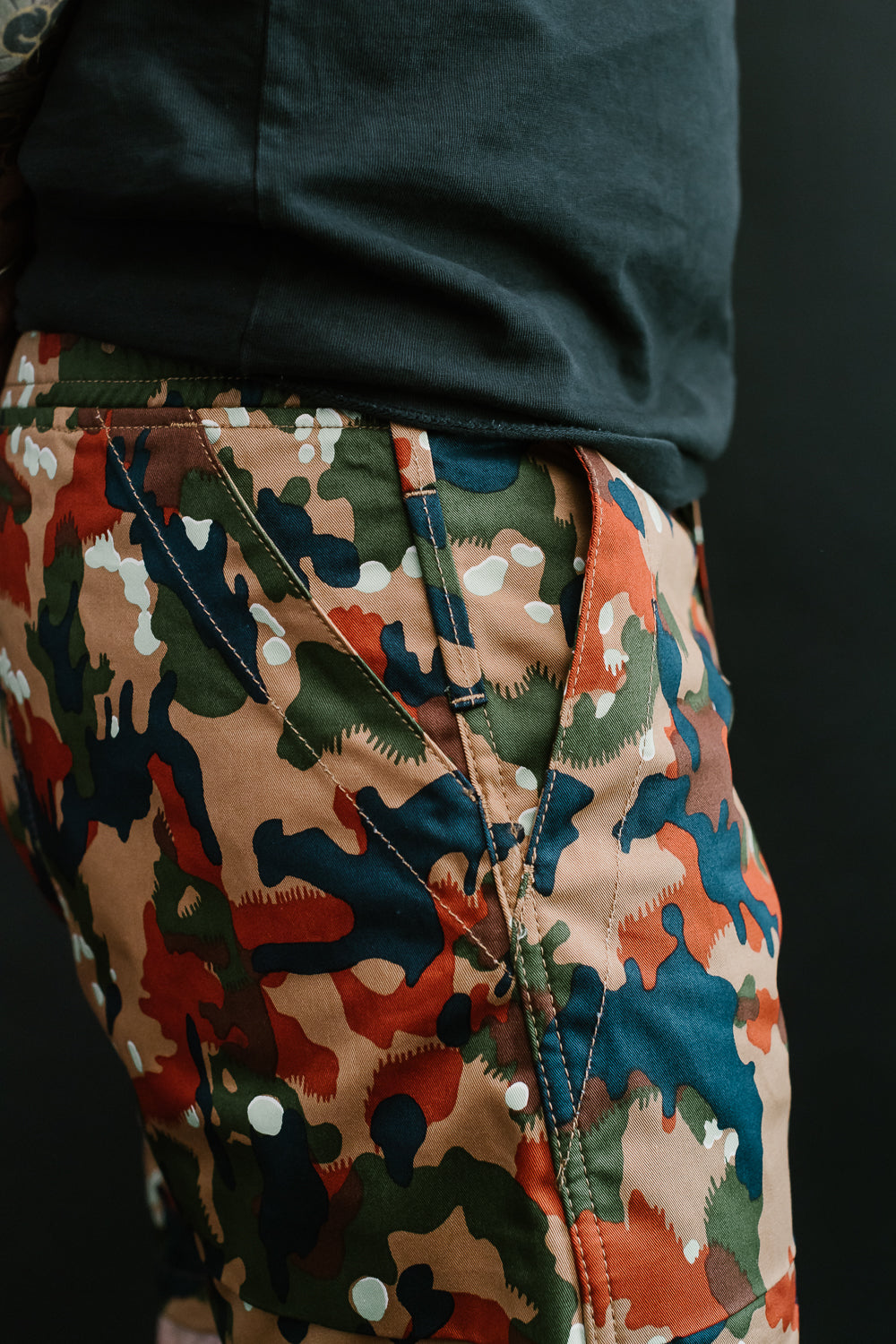 Close-up front view of men's camouflage shorts with colorful print, diagonal stitching, and side pocket detail on athletic model.