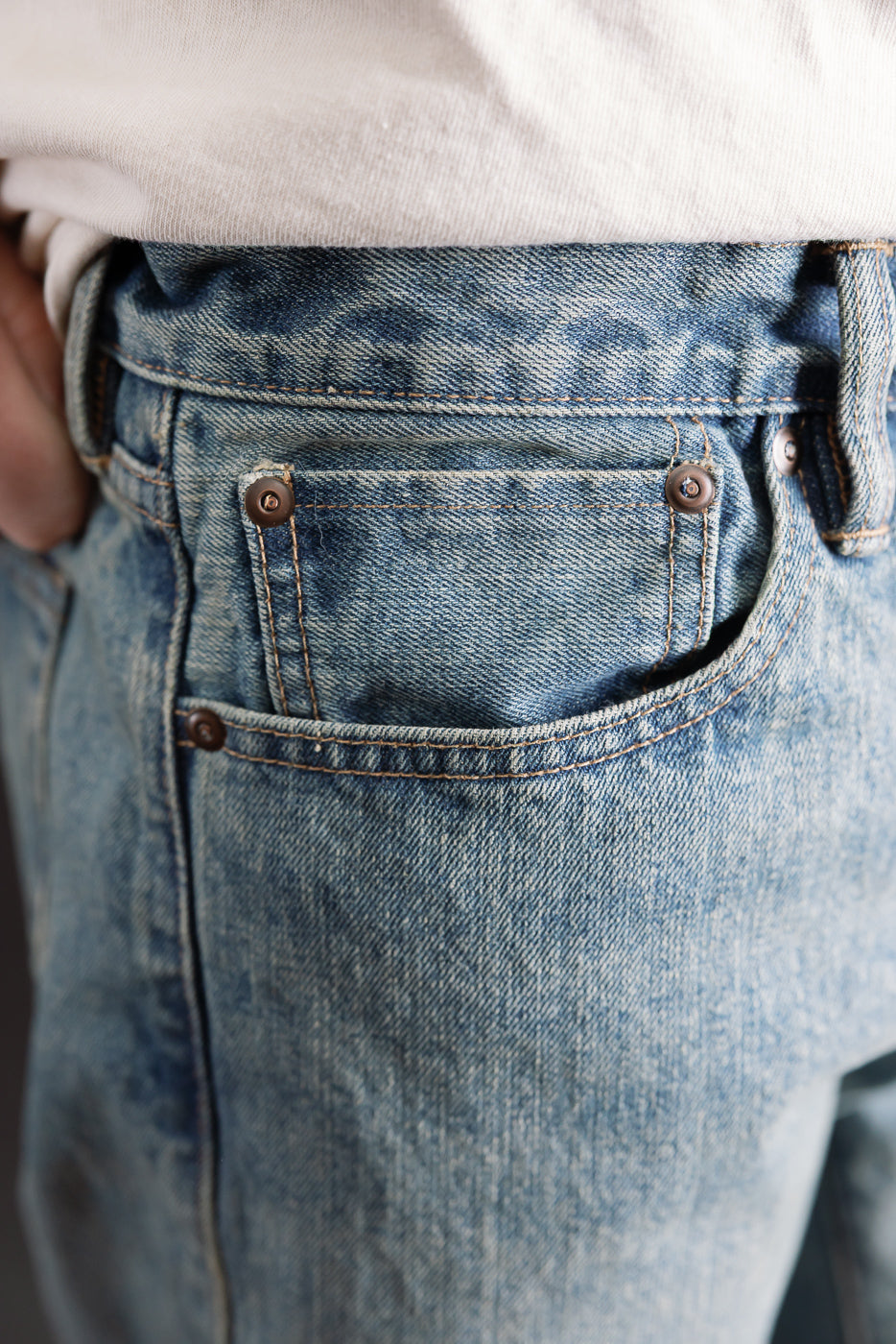 Close-up of front right pocket and coin pocket, indigo river-washed selvedge jeans on male model, showing denim texture and rivet details.