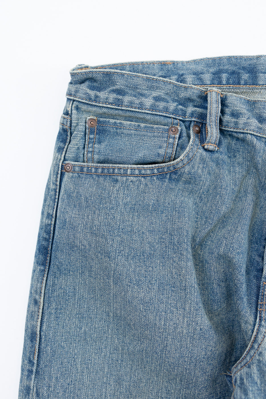 Close-up of front left pocket and waistband, indigo river-washed selvedge denim jeans, showing rivet details and texture.