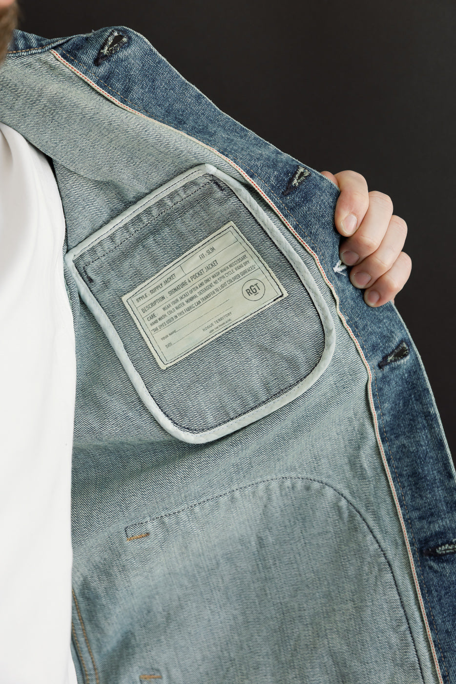 Close-up of male model's denim jacket interior, showing RGT tag, pocket, and stitching details.