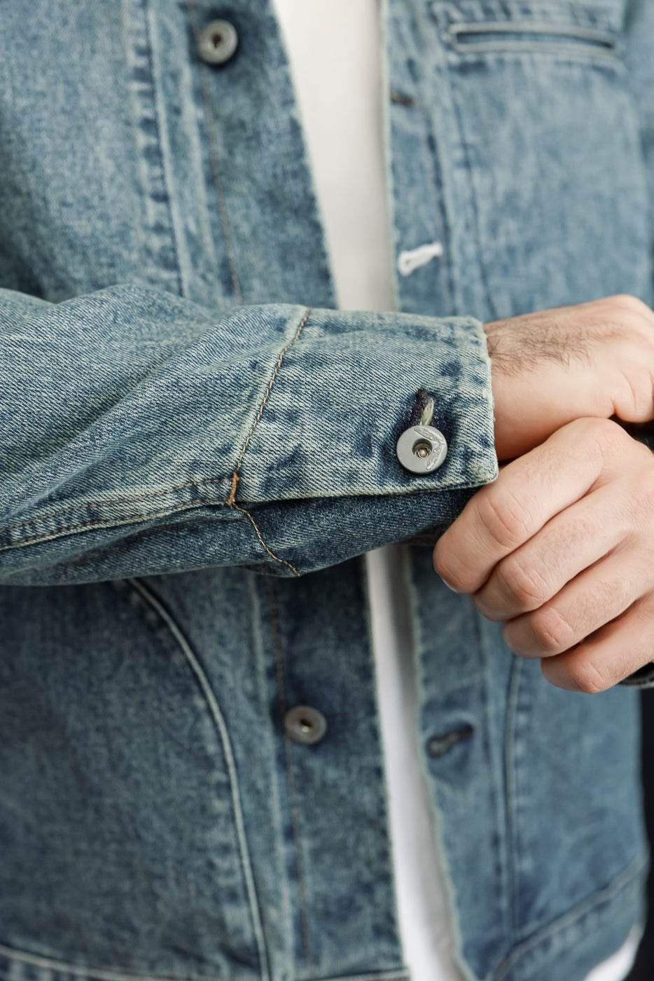 Close-up of male model's denim jacket sleeve, showing button cuff and fabric texture, front view