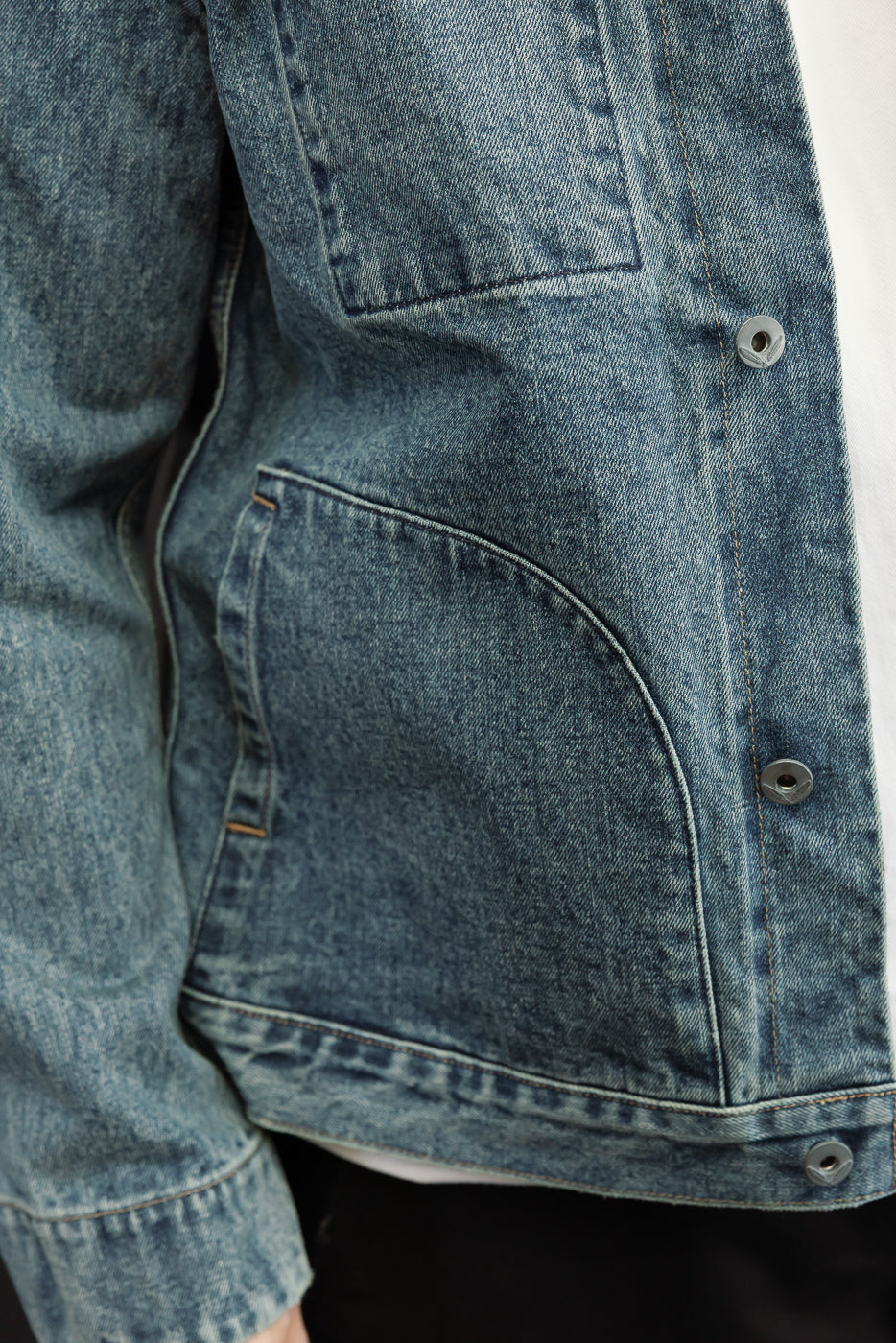 Close-up of male model's denim jacket front, showing button details, pocket stitching, and fabric texture.
