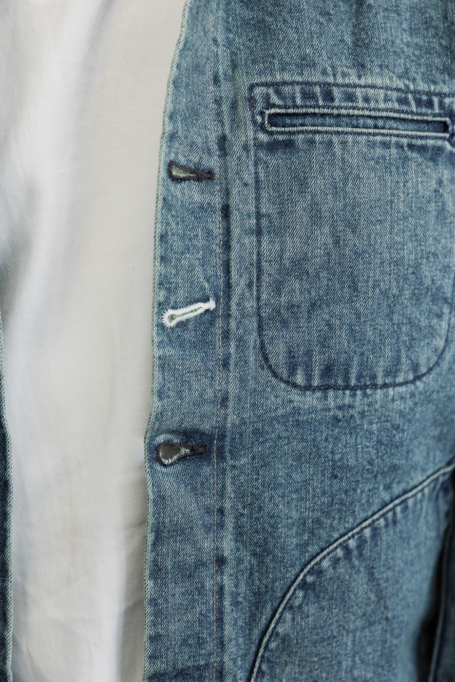 Close-up of male model's denim jacket front, showing buttonholes and pocket detail, athletic build.