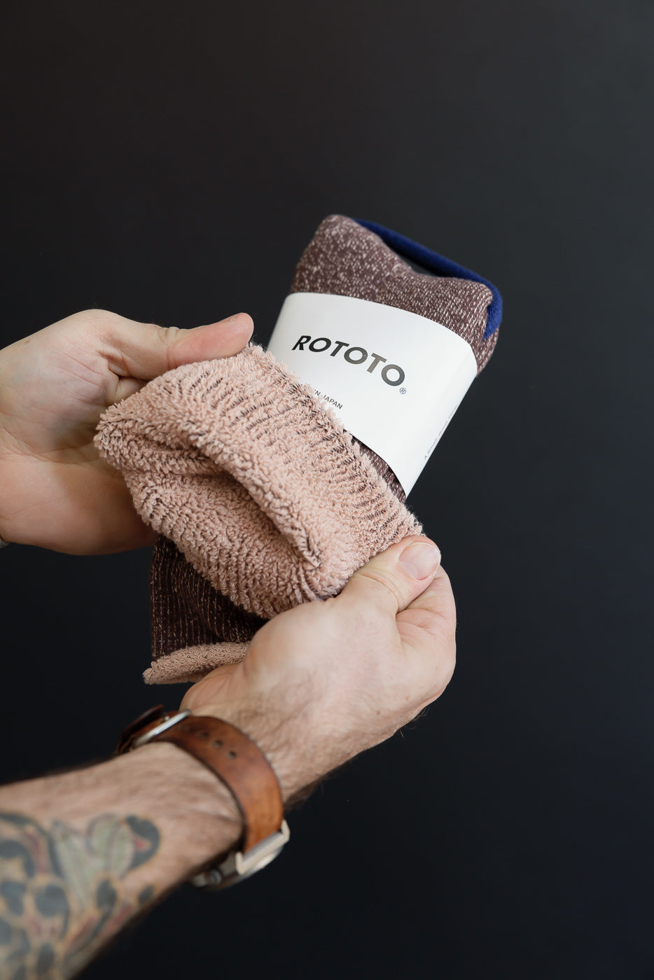 Close-up of a person's hands holding a pair of textured brown ROTOTO socks.