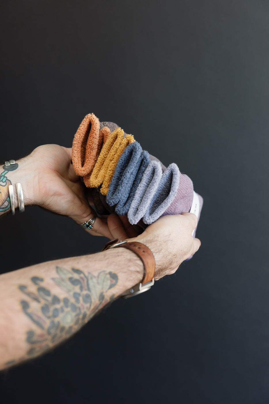 Close-up of a male model's hands holding a stack of folded colorful selvedge fabric towels.