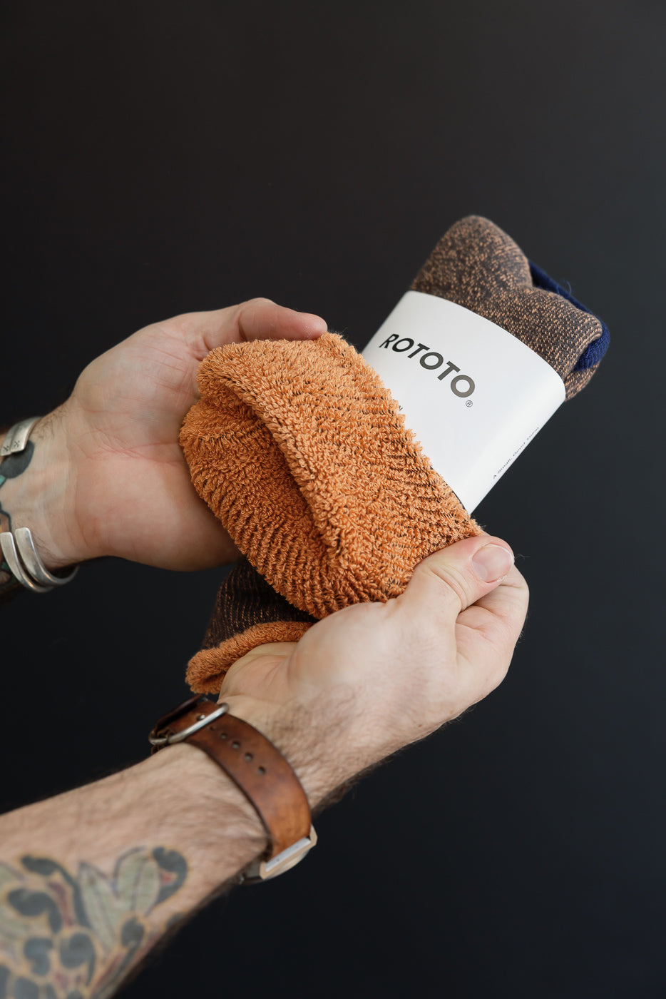 Close-up of a male's hands holding a pair of textured orange and brown ROTOTO socks.