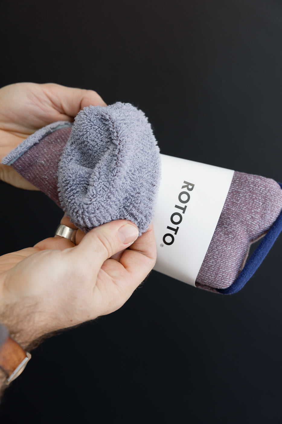Close-up of hands holding a textured purple Rototo sock with a white branded band.