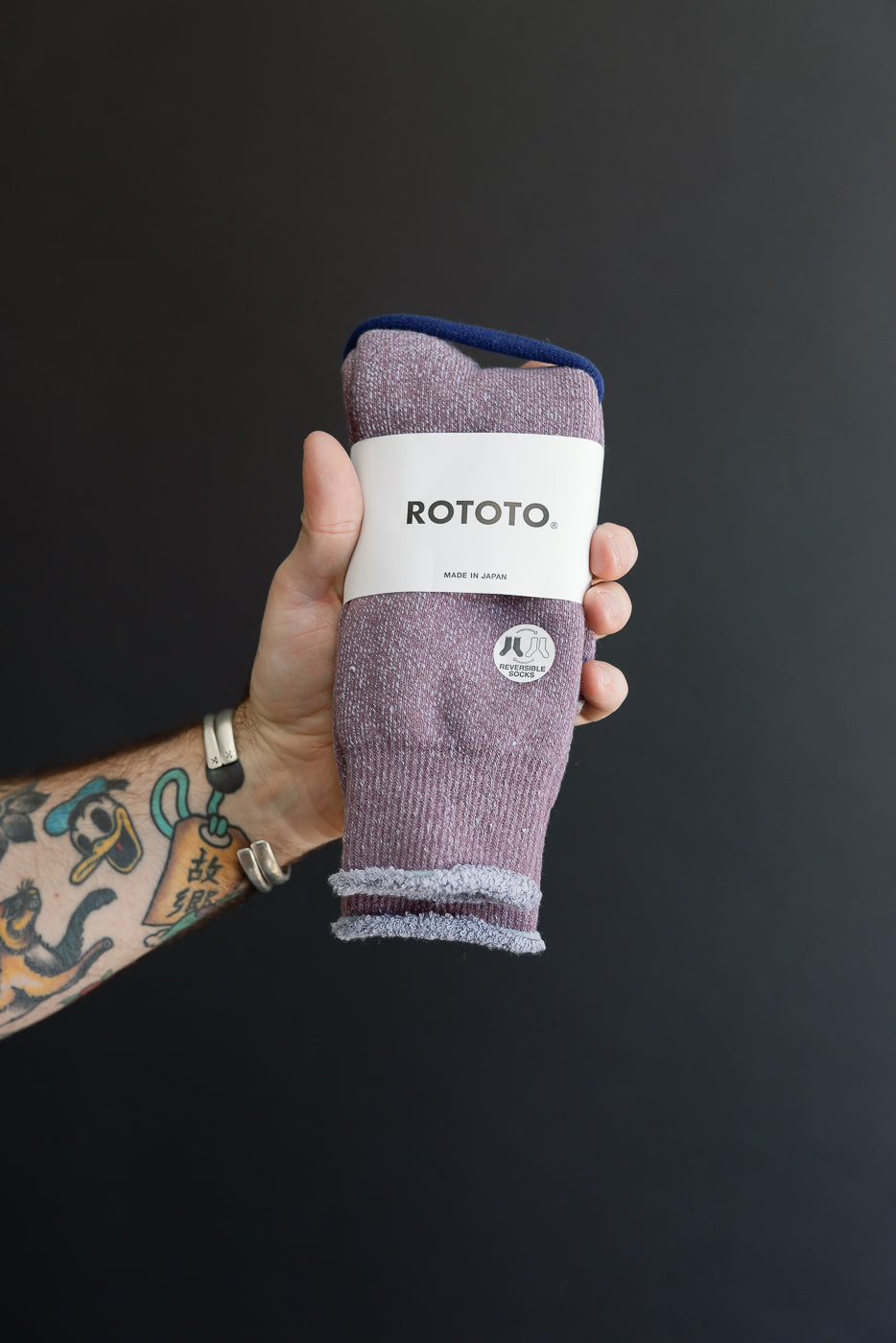 Close-up of a hand holding a pair of purple ROTOTO reversible socks with a white paper band.