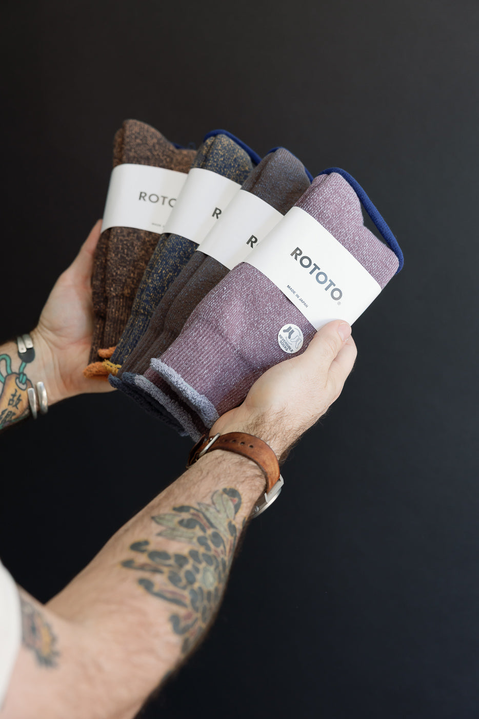 Hands holding a stack of four Rototo knit beanies in various colors, front view.