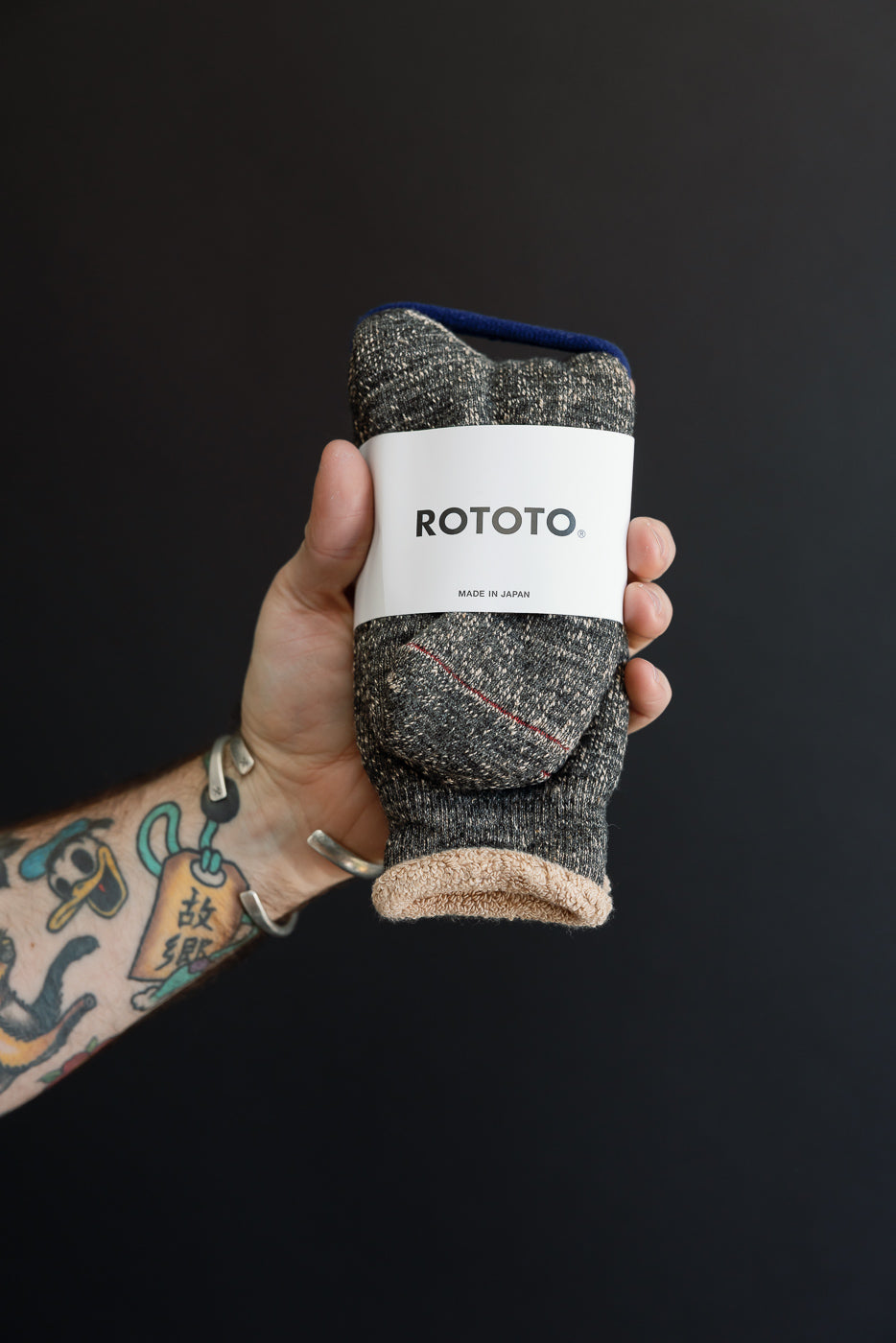 Close-up of a hand holding a pair of grey ROTOTO socks with a white product label.