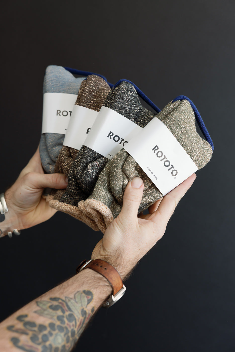 Close-up of a person's hands holding four pairs of folded Rototo socks in various colors.