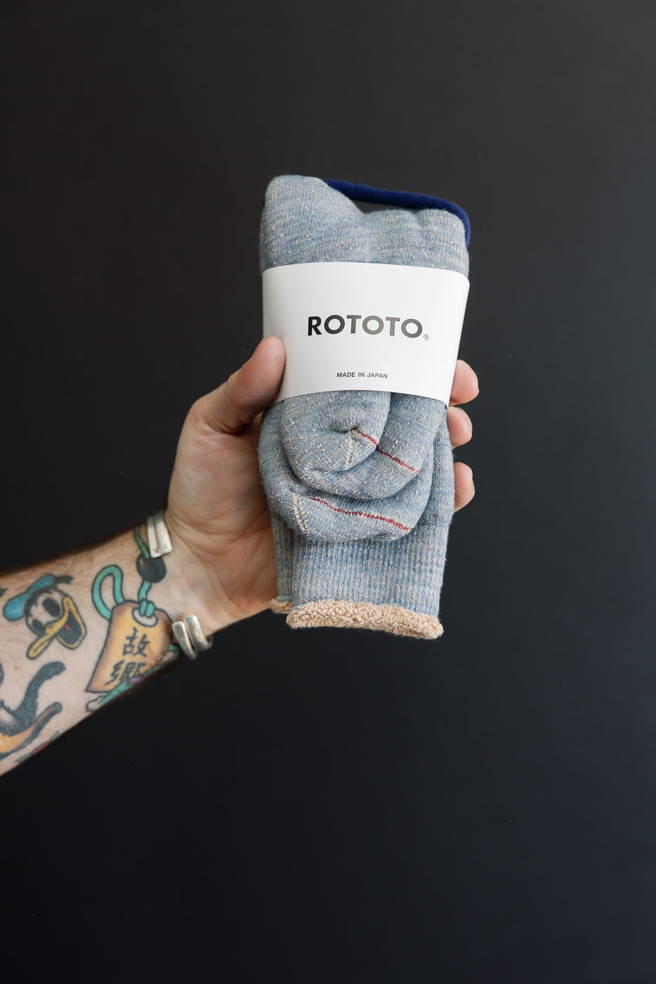 Close-up of the front of a rolled pair of grey melange knit socks with a white ROTOTO band.