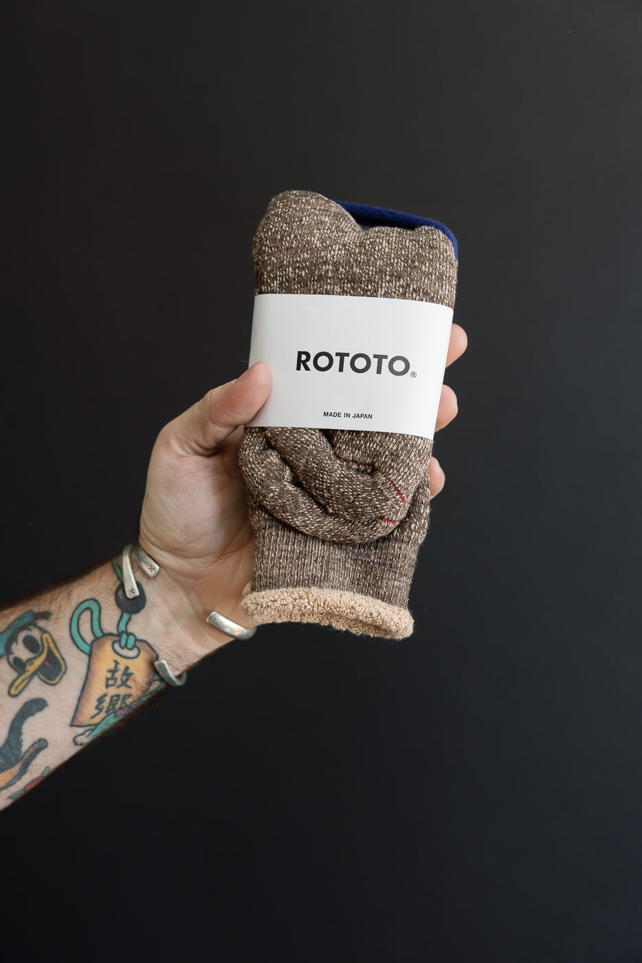 Close-up of a male's hand holding brown ROTOTO socks with a white paper band.