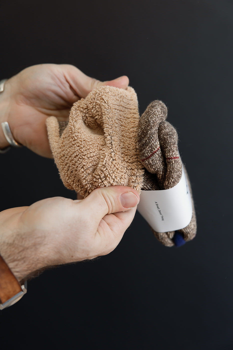 Close-up of hands holding textured tan and brown patterned knit socks with a white paper band.