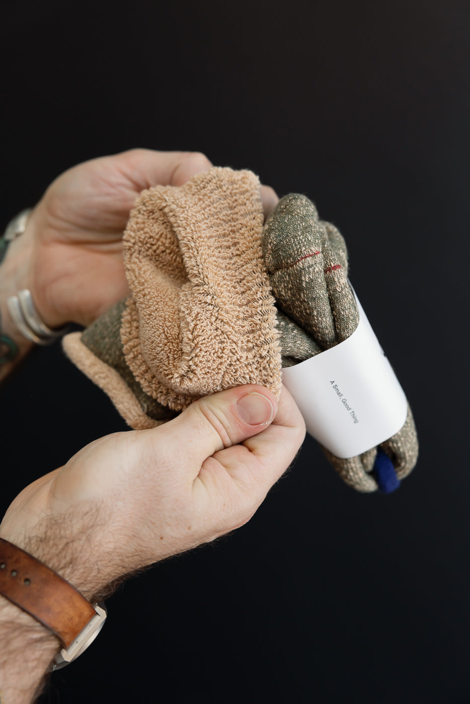 Close-up of a hand holding a textured, tan and olive green terry cloth towel with a white tag.