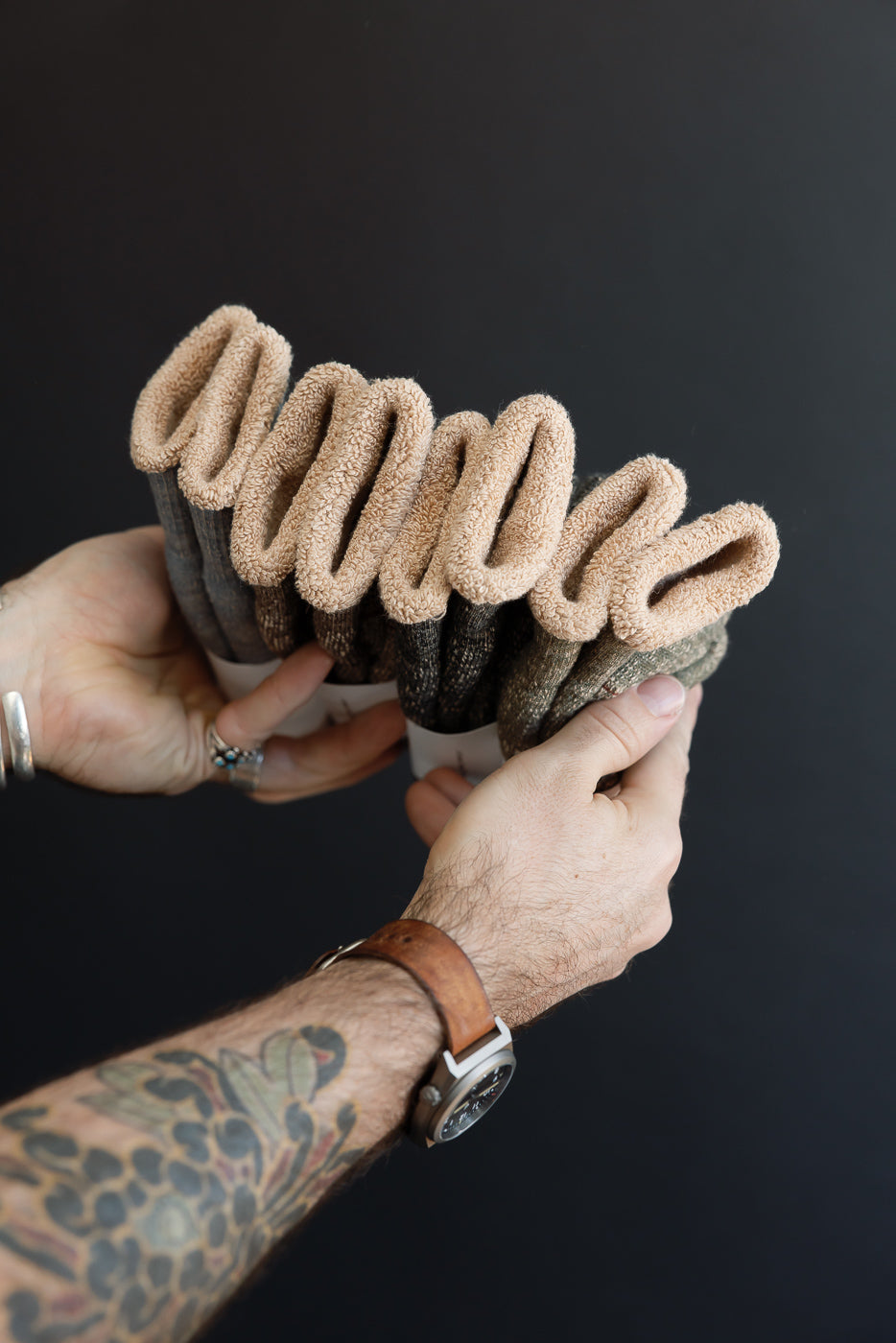 Close-up of a person's hands holding a stack of folded brown textured fabric rolls.