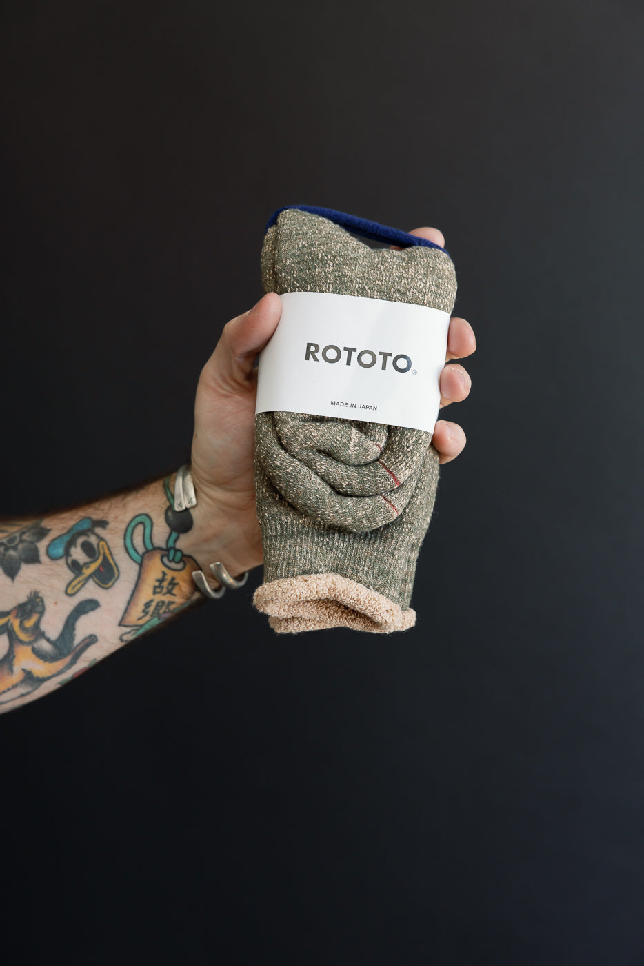 Close-up of a male hand holding rolled ROTOTO socks, showing the fabric texture and brand tag.