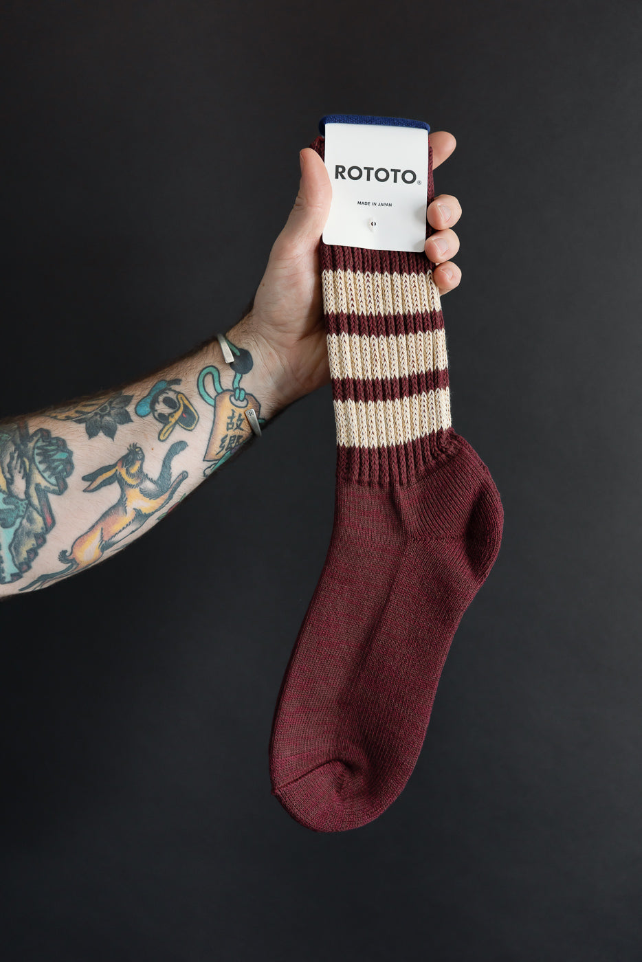 Close-up of the front of a maroon and cream striped Rototo sock held by a male hand.