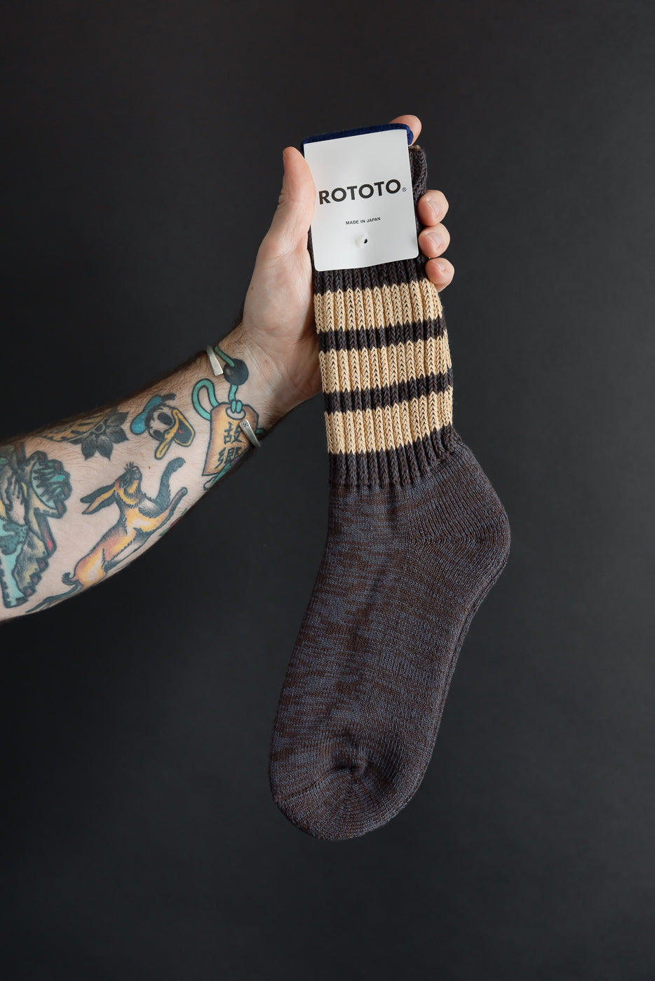 Close-up of the front of Rototo striped knit socks held by a hand against a black background.