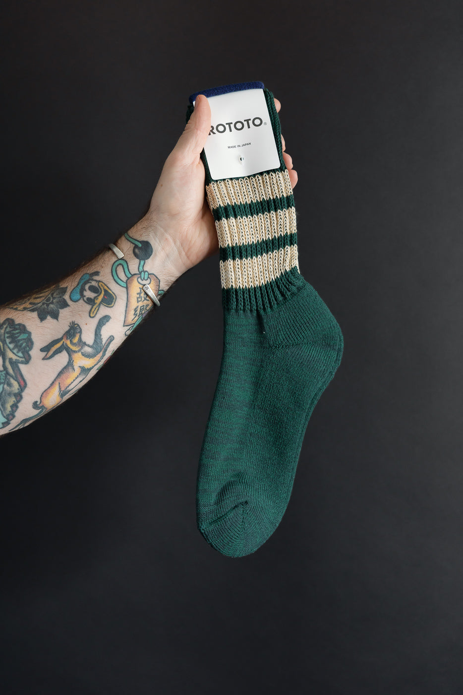 Close-up of the front of a green and tan striped Rototo sock held by a male hand.