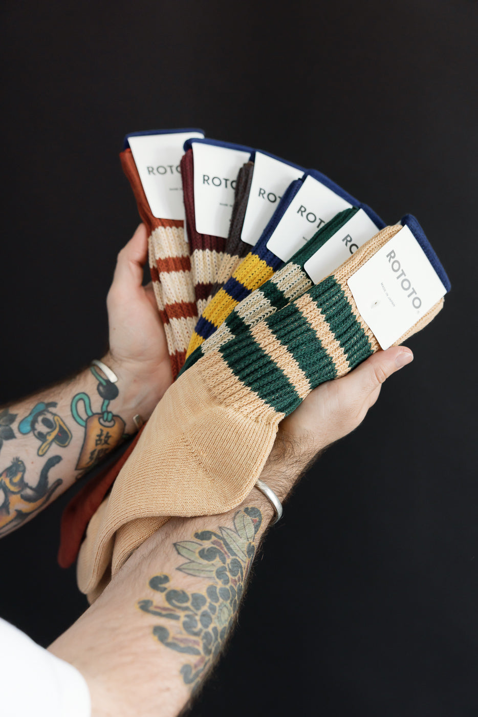 Close-up of a male model's hands holding a fan of colorful striped ROTOTO socks.