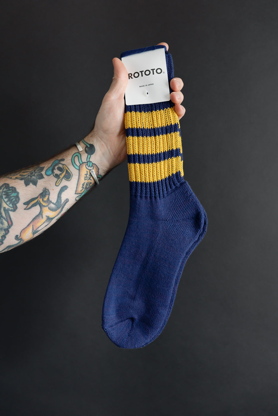 Close-up of a male's hand holding a blue and yellow striped ROTOTO sock, showing the tag.