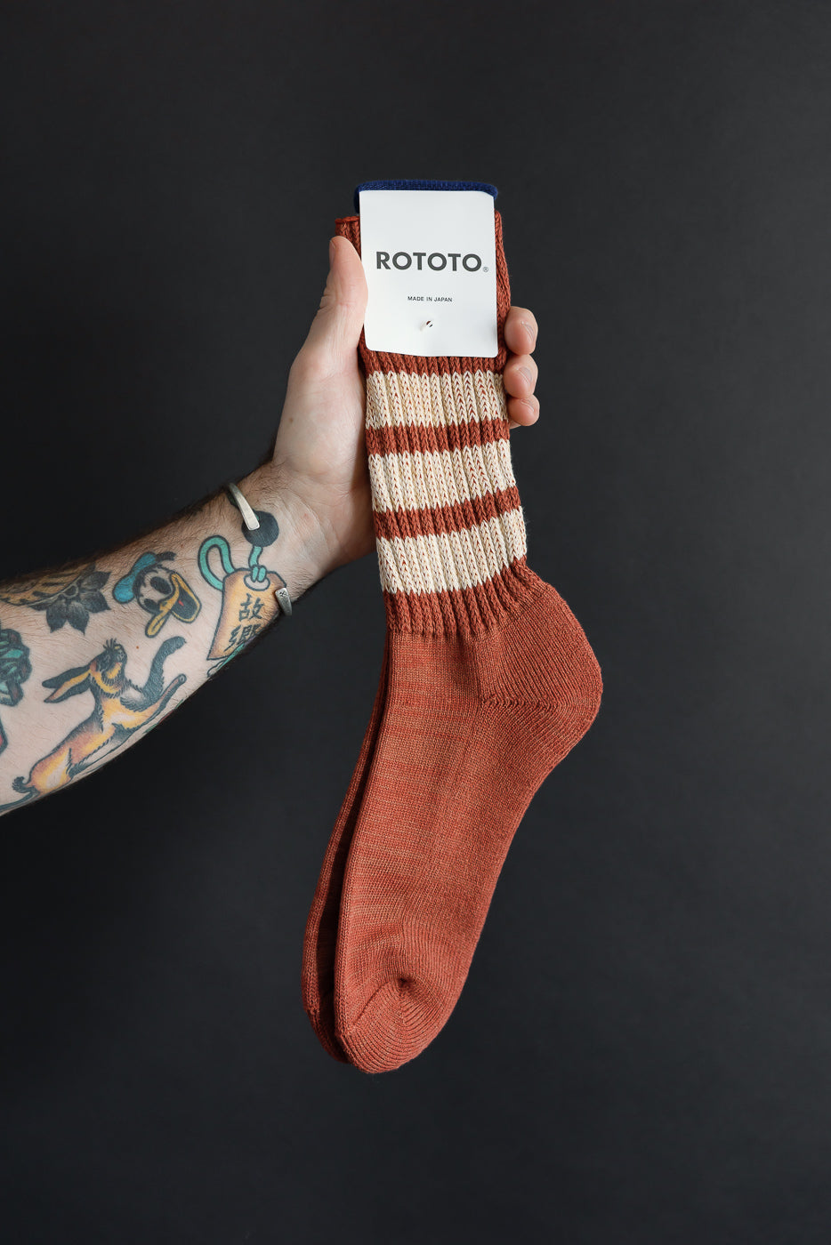 Close-up front view of striped terracotta and cream ribbed knit socks held by a hand.