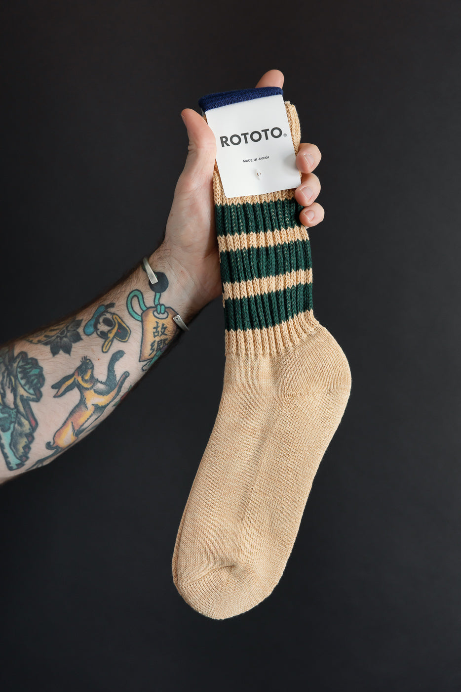 Close-up front view of tan and green striped Rototo socks held by hand.