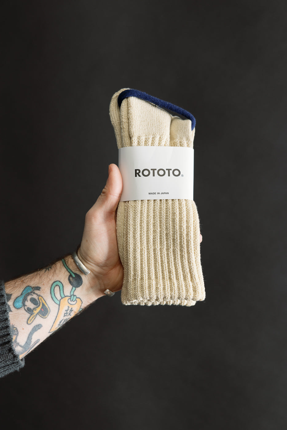 Close-up of packaged raw beige crew socks, front view, ribbed knit detail, held in hand