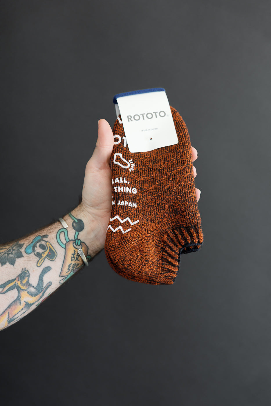 Close-up of the front of an orange Rototo sock with white text and a brand tag held by a male hand.