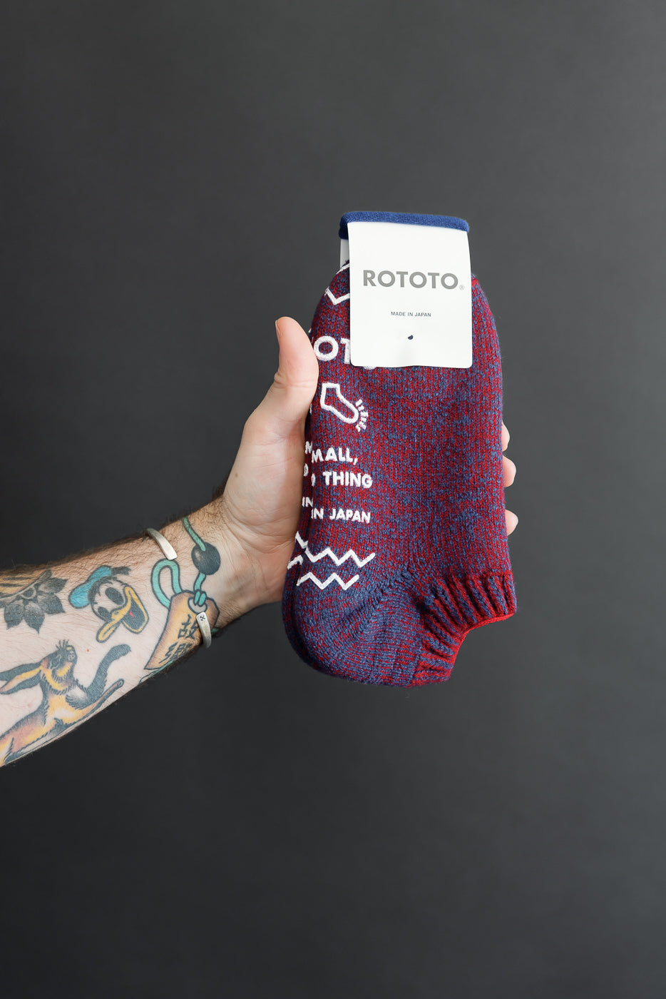 Close-up of the front of a patterned Rototo sock held by a person's tattooed hand.