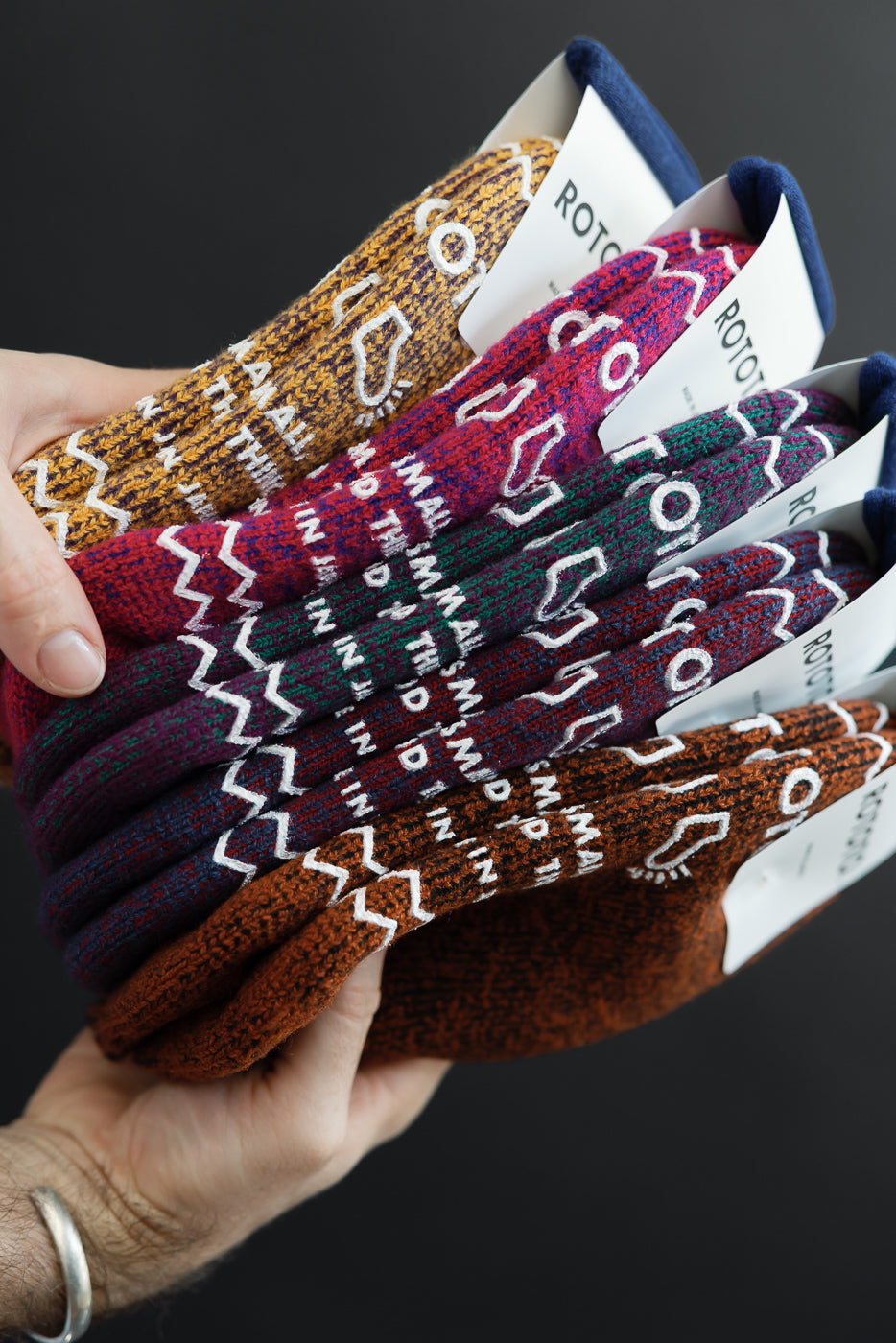 Close-up of a male's hand holding a variety of patterned knit socks, showing fabric texture and tags.