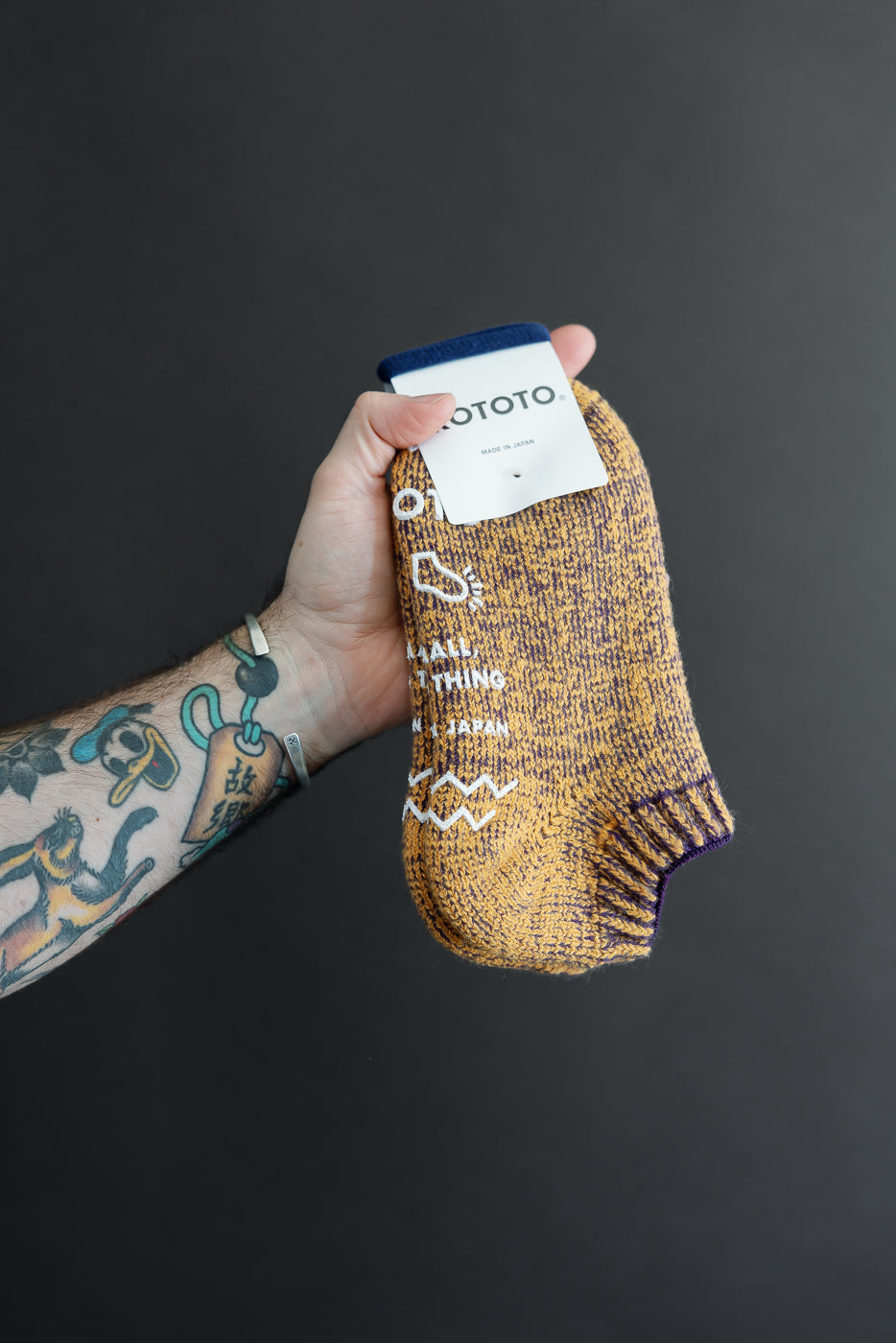 Close-up of a male hand holding a yellow textured sock showing the front and brand tag.