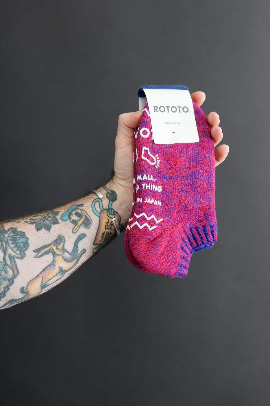 Close-up of the side of a pink and blue patterned Rototo sock held by a male hand.