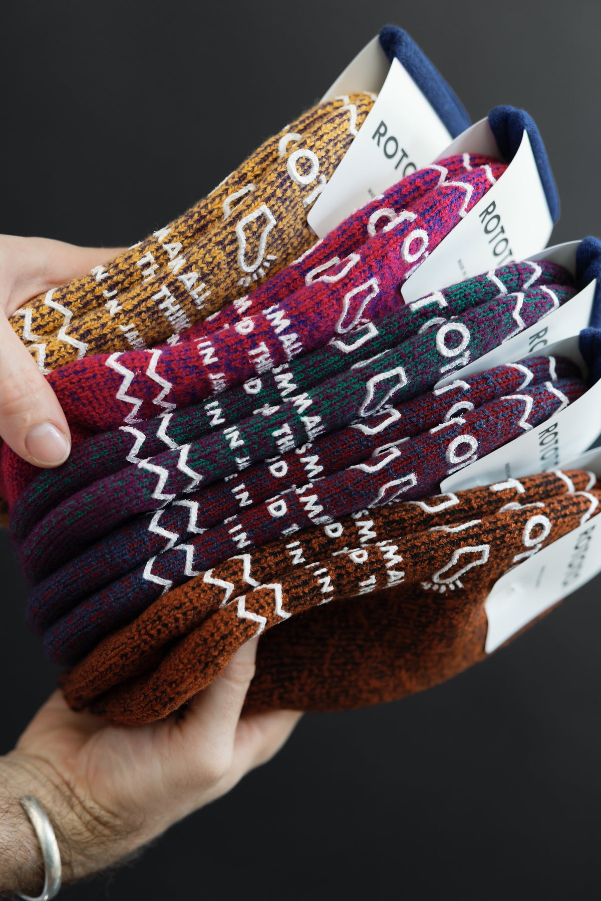 Close-up front view of patterned knit socks in multiple colors held in a hand.
