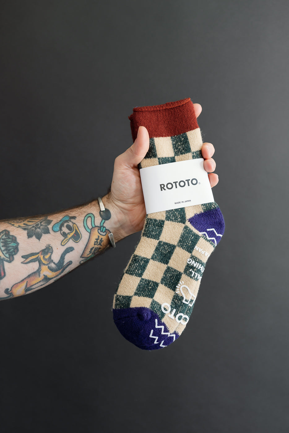 Close-up of the front of a tan and navy checkered Rototo sock held by a hand.