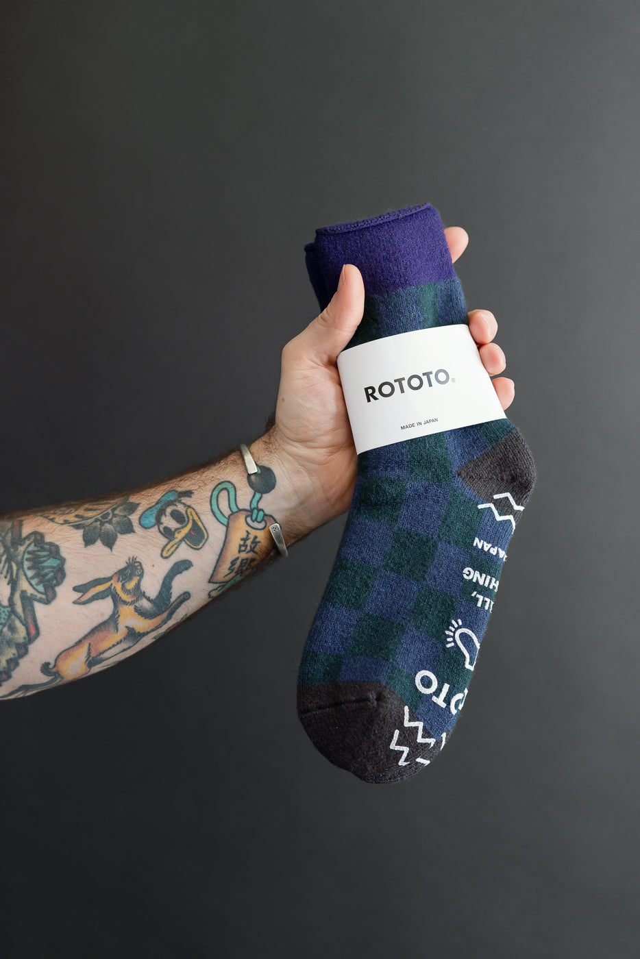 Close-up of a male hand holding a pair of blue and dark green checkered ROTOTO socks.