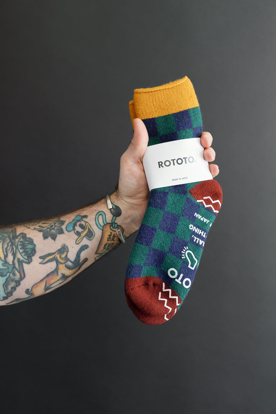 Close-up of a hand holding a pair of ROTOTO checkered socks with yellow, green, and burgundy colors.