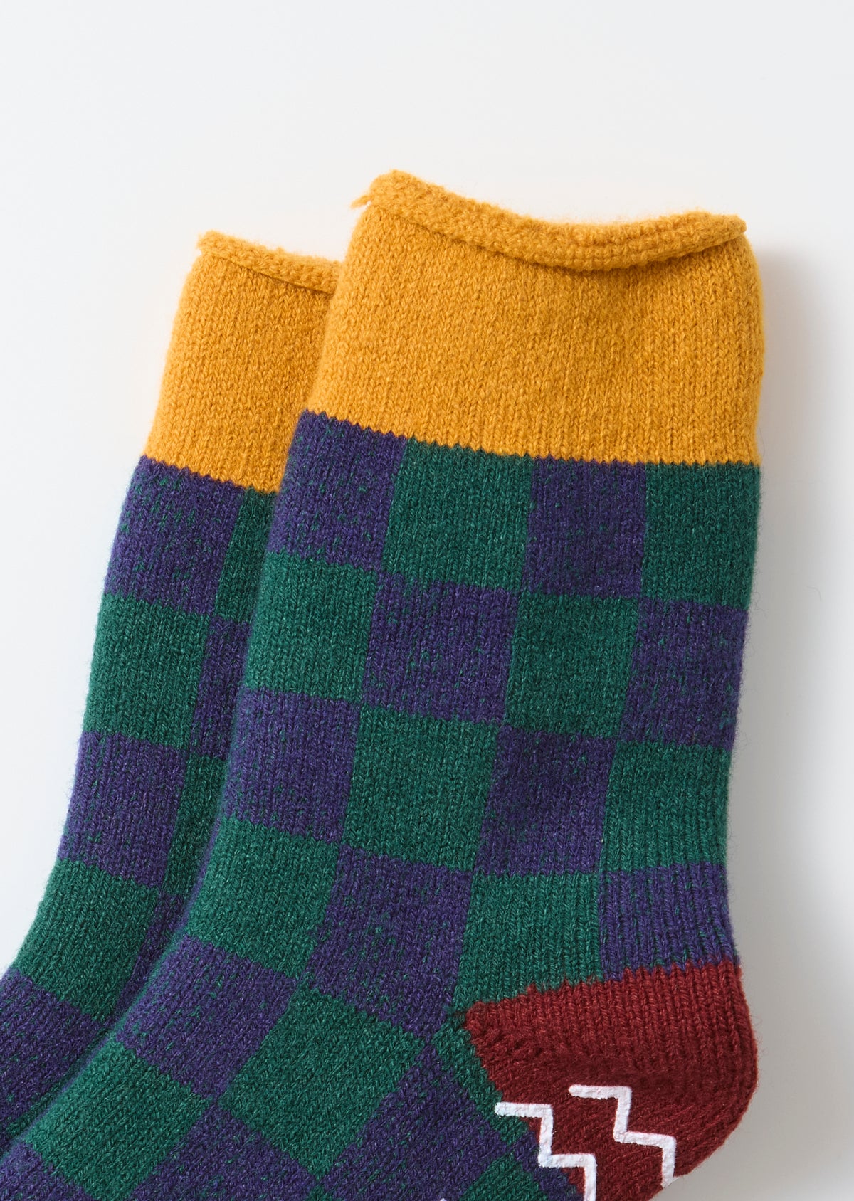 Close-up flat lay of the front of green and purple checkered socks with yellow cuffs.